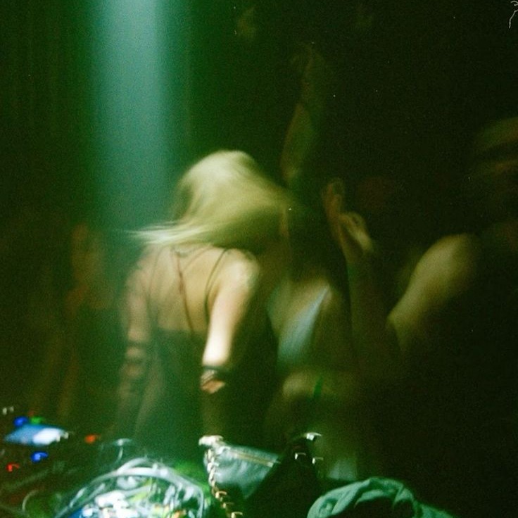 Green-lit room with a DJ setup and dancers in motion
