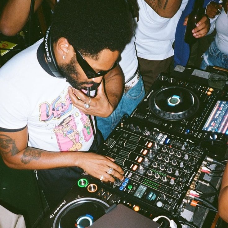 A DJ leaning into the decks mid-set, surrounded by the crowd.