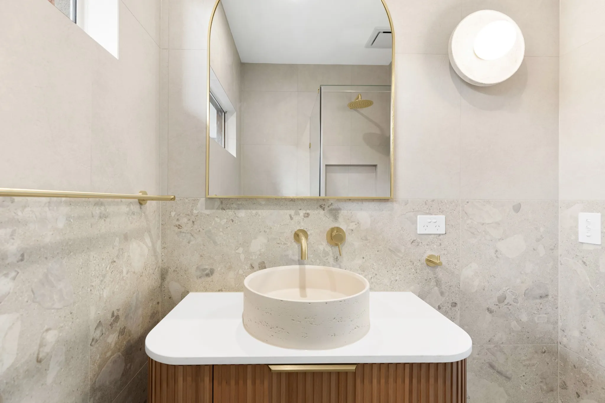 Organic Curves powder room with a stone vessel basin, brushed-brass tapware and terrazzo splashback