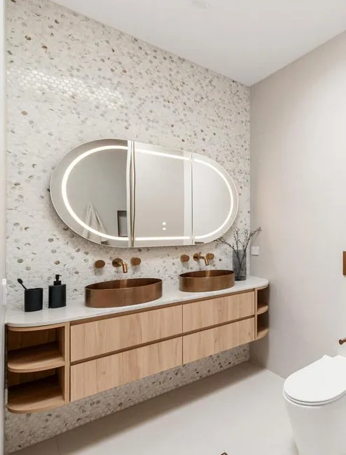Bronze Age ensuite with a pebble-mosaic wall, an oval lit mirror, copper basins and a curved timber vanity