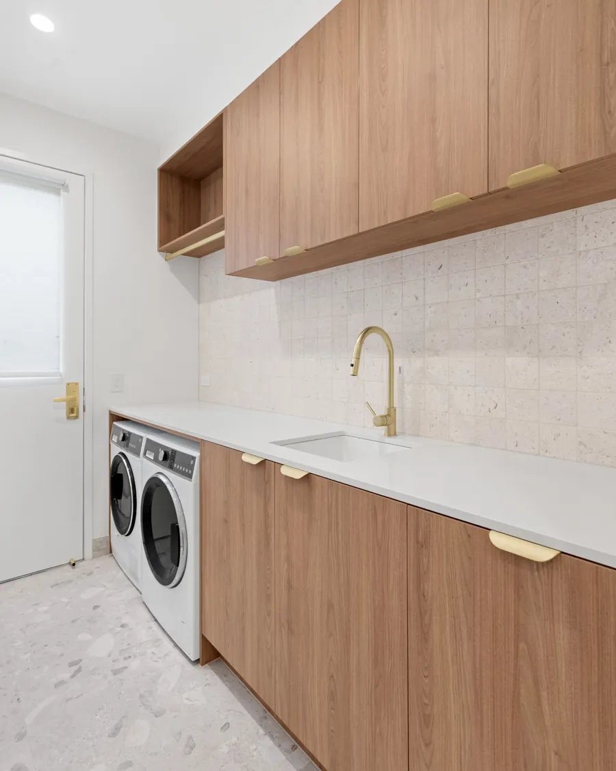 Organic Curves laundry with timber cabinetry, a handmade tile splashback and brushed-brass tapware