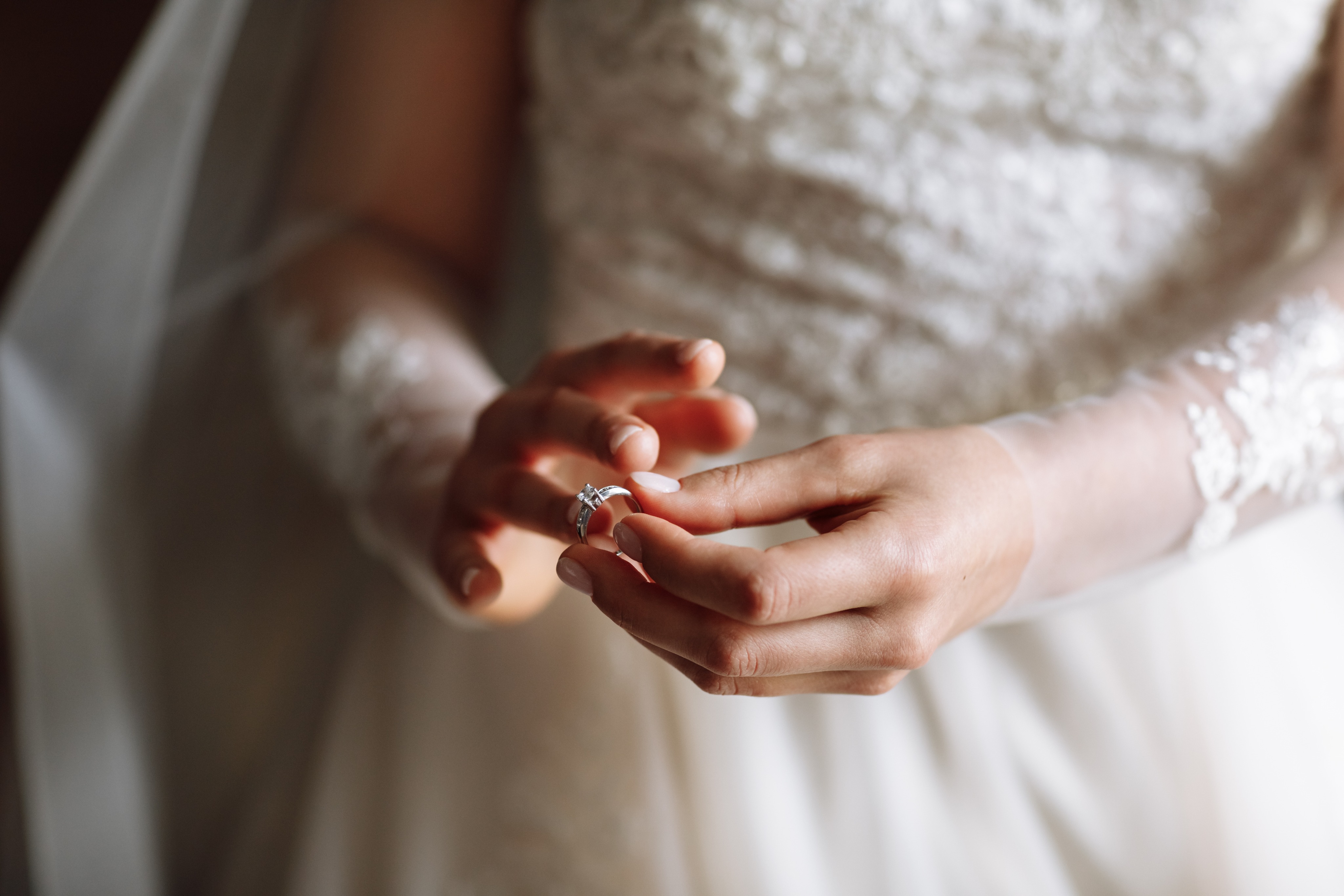 A bride in a lace-sleeved gown touching her diamond engagement ring