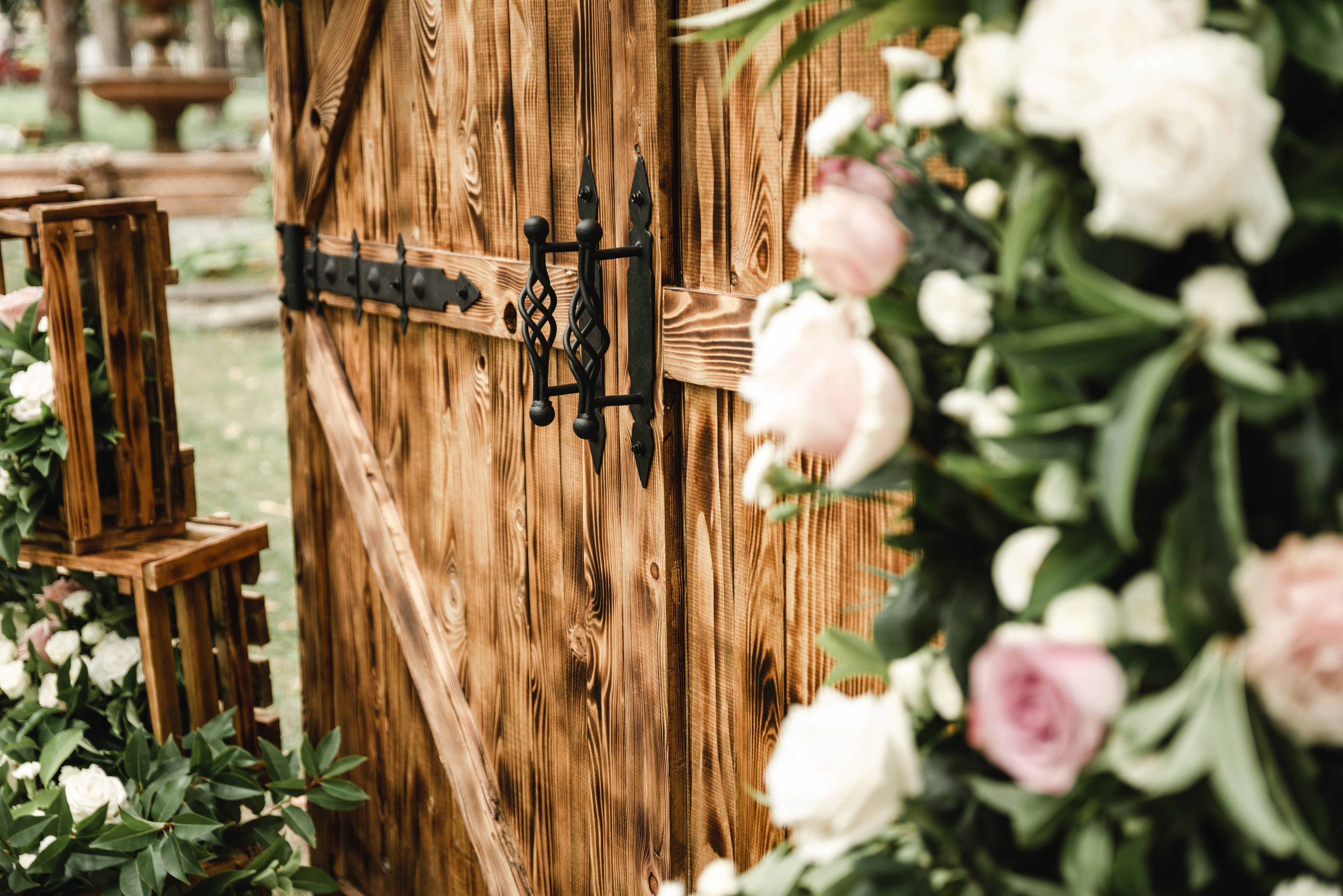 Rustic timber ceremony doors with black iron hardware, framed by blush and ivory roses